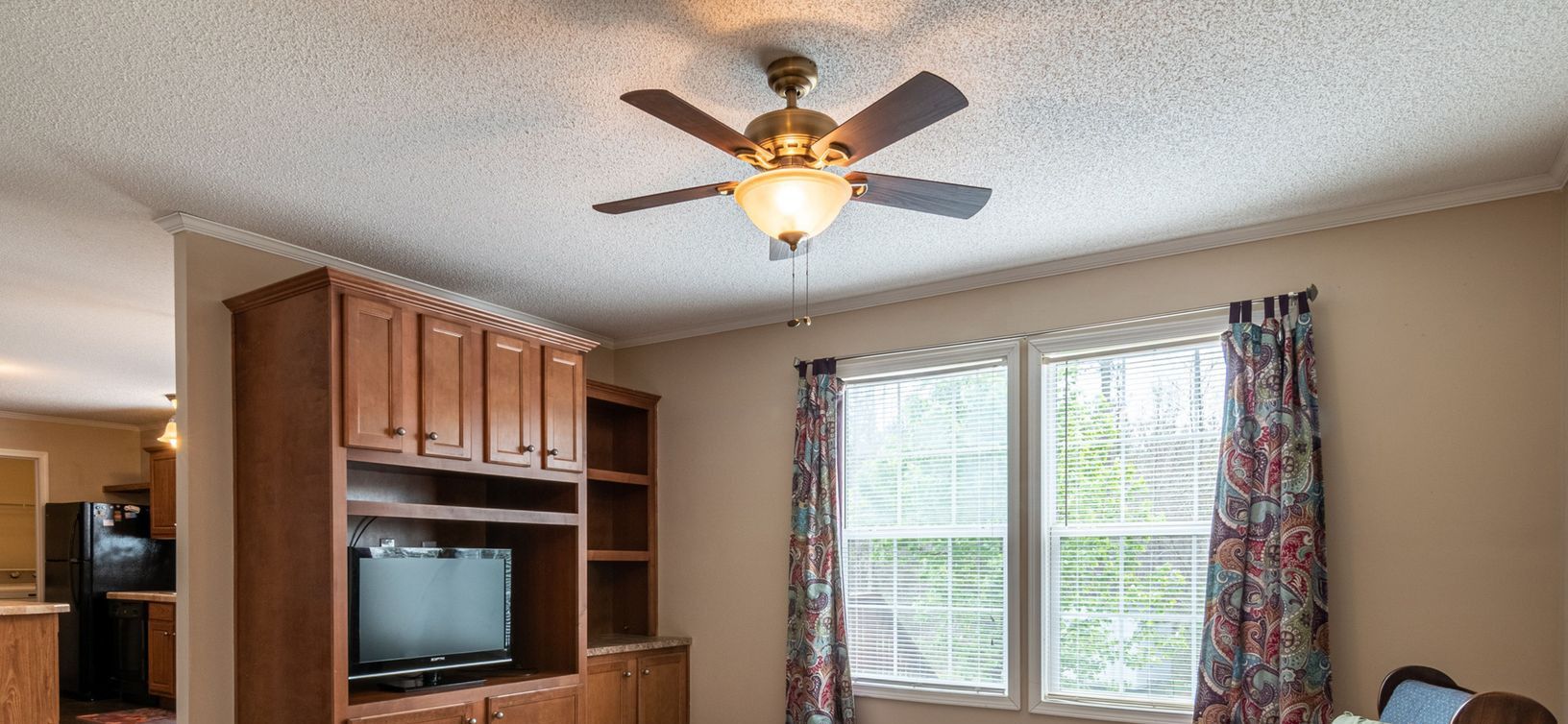 Spacious living room with classic wooden entertainment center and ceiling fan, perfect for a family setting.